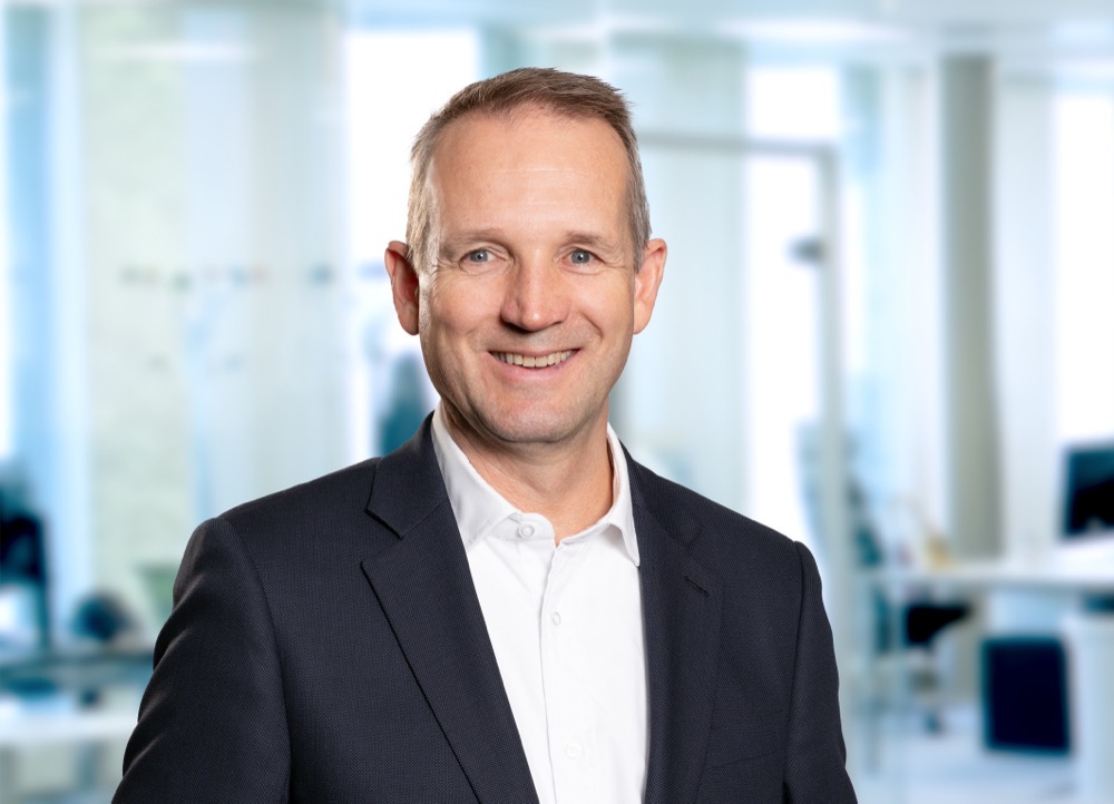 Jan Sølvberg i mørk dress, smilende, på et lyst kontor